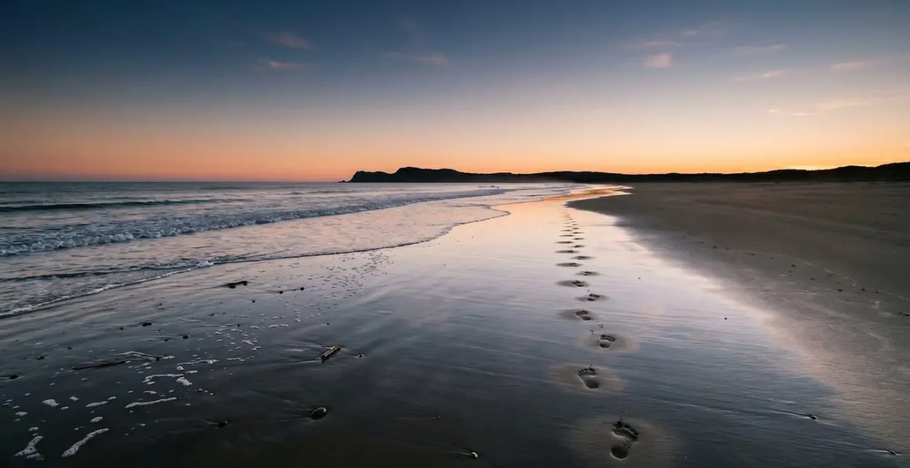 Deserted beach at golden hour with single set of footprints along water's edge