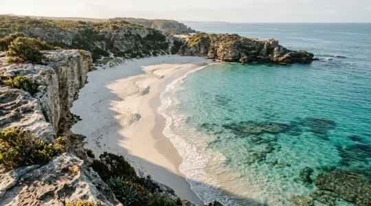 Pristine private beach cove with crystal clear turquoise waters and white sand between dramatic cliffs
